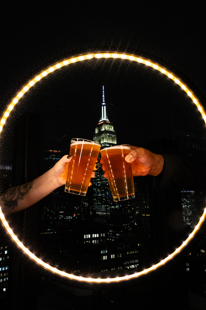 two beers clinking glasses in front of the empire state building